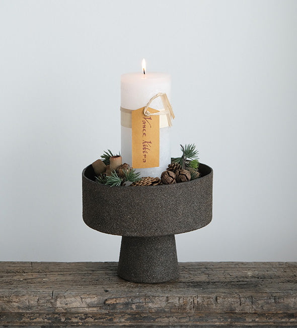 Decorative candle holder with a candle and pinecones on a wooden surface