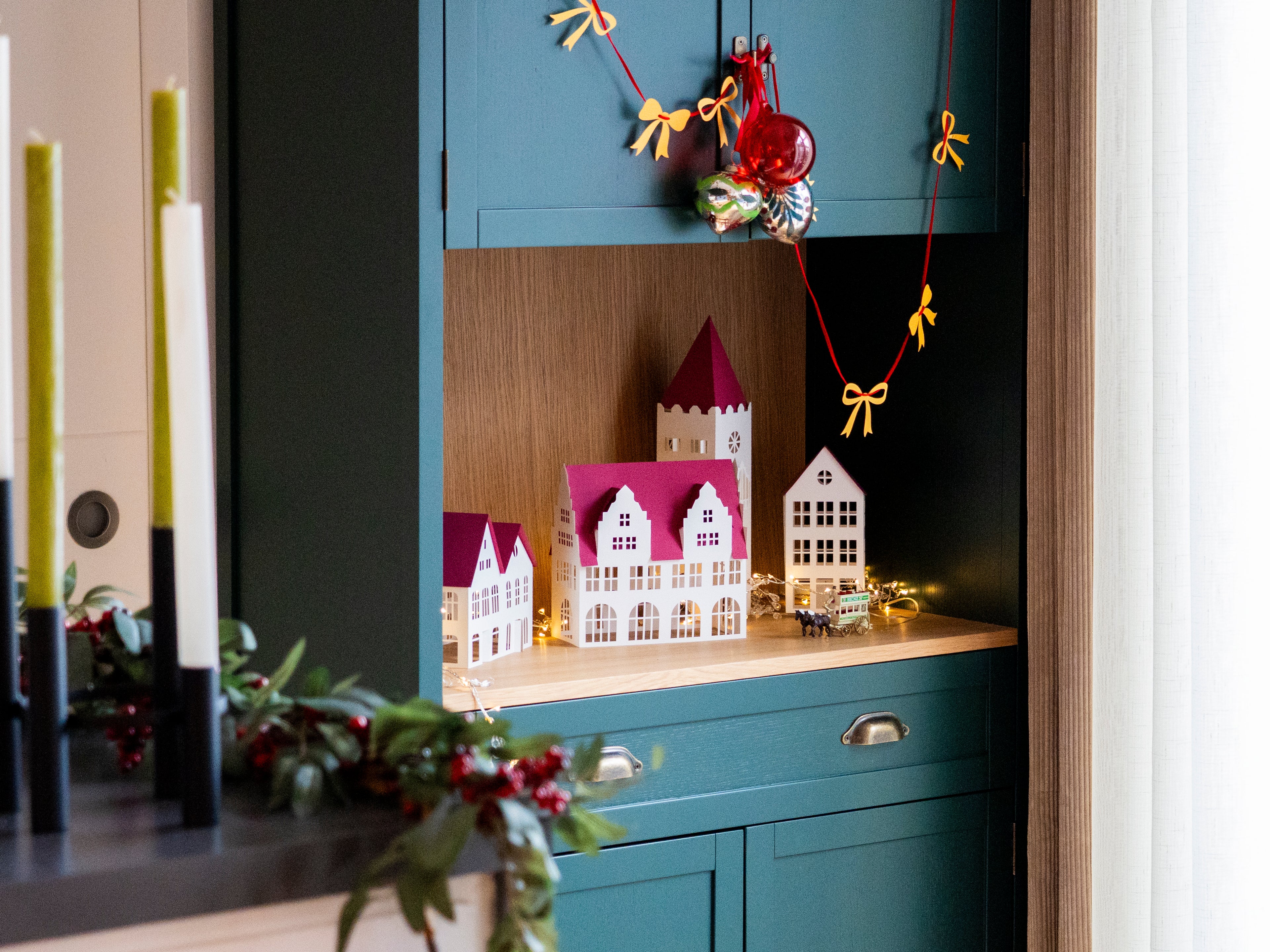 Decorative display of christmas village houses and a colorful wreath on a shelf.