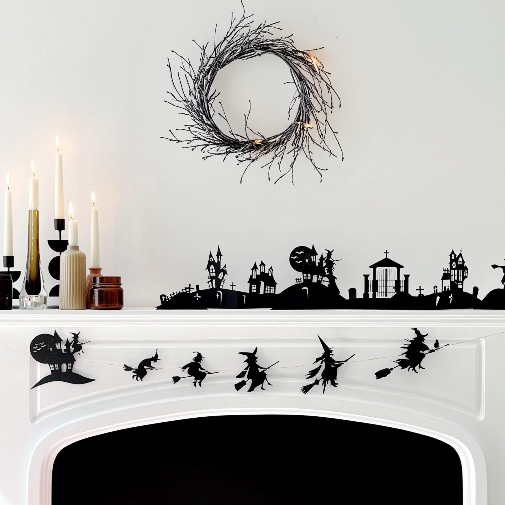 A Halloween-themed garland displayed on a fireplace mantle, featuring silhouettes of witches, a haunted house, and bats against a moonlit skyline backdrop.