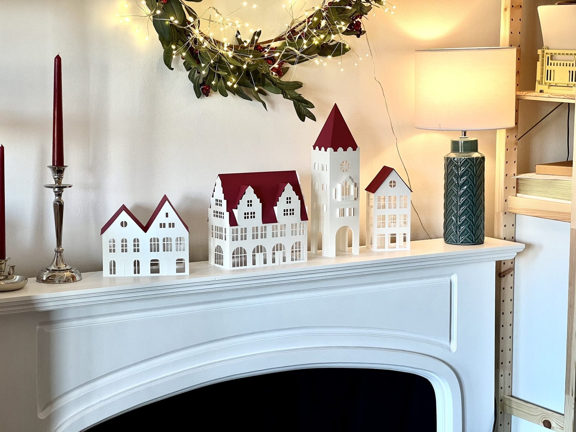 A modern, minimalist paper Christmas village by Norrska displayed on a sleek mantelpiece with warm backlighting.