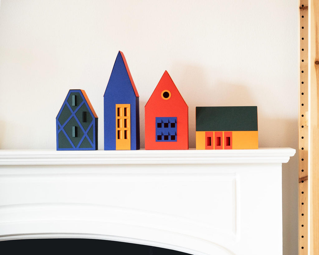Colourful paper houses on a white fireplace mantel next to a bookshelf.