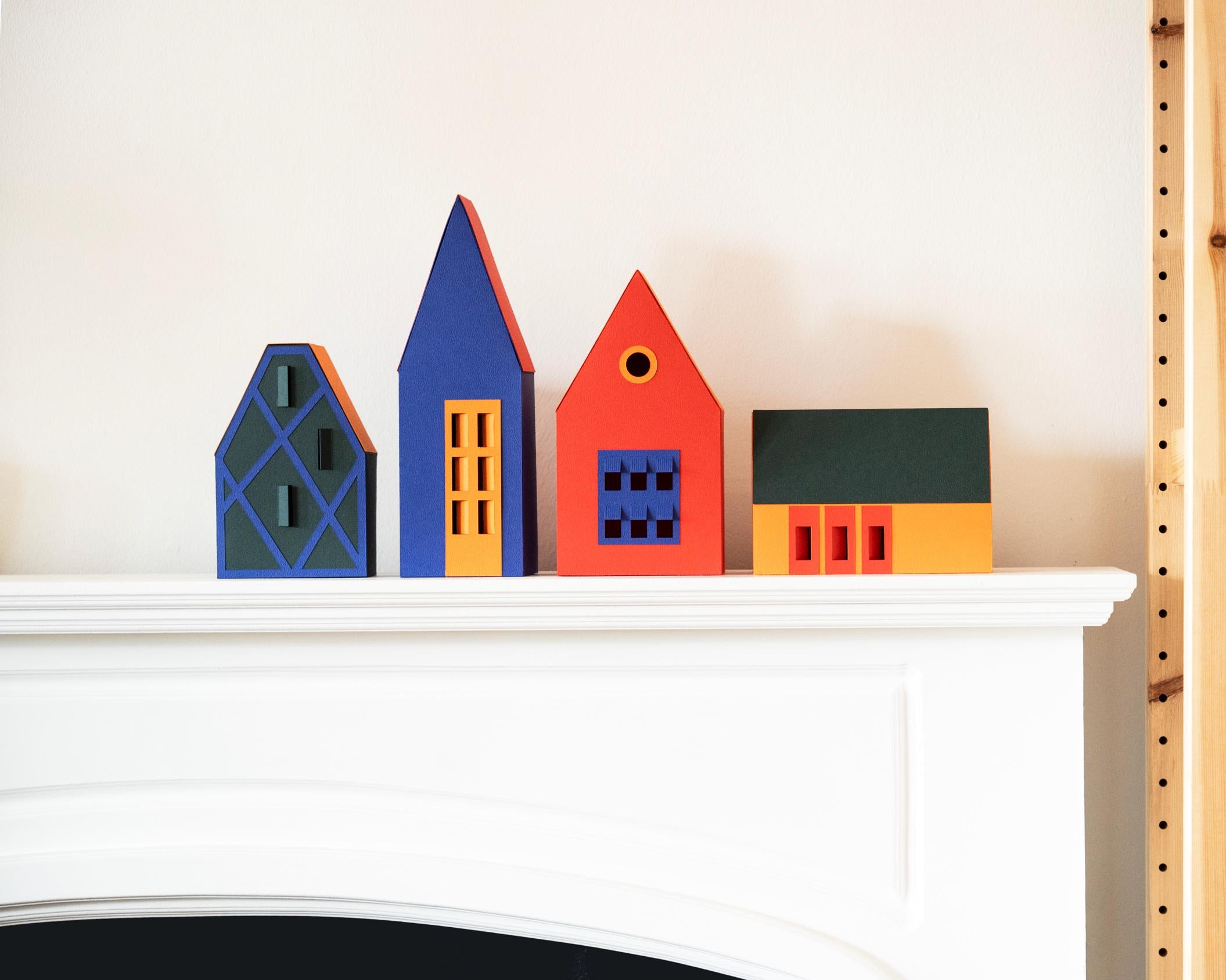 Colourful paper houses on a white fireplace mantel next to a bookshelf.
