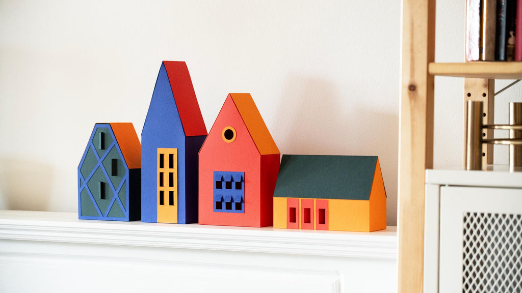 Colourful paper house models on a shelf against a white wall