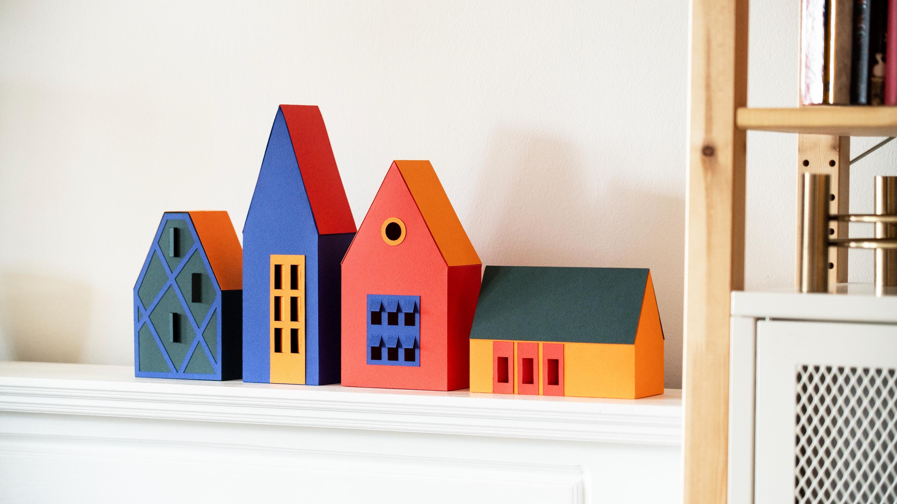 Colourful paper house models on a shelf against a white wall