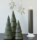 Decorative paper Christmas trees and a tall candle on a reflective surface with a light gray background