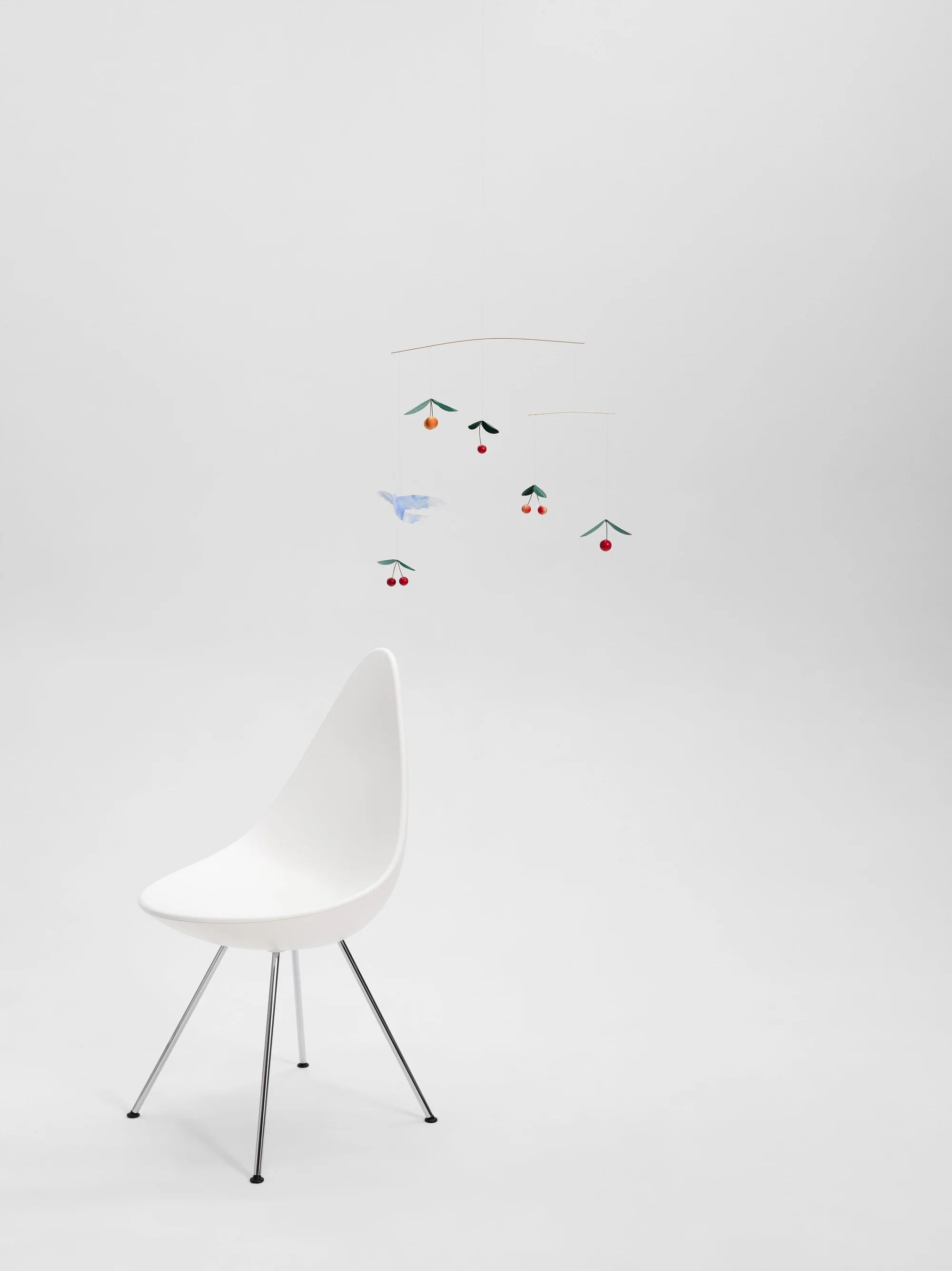 White chair with a colorful mobile hanging above it on a white background