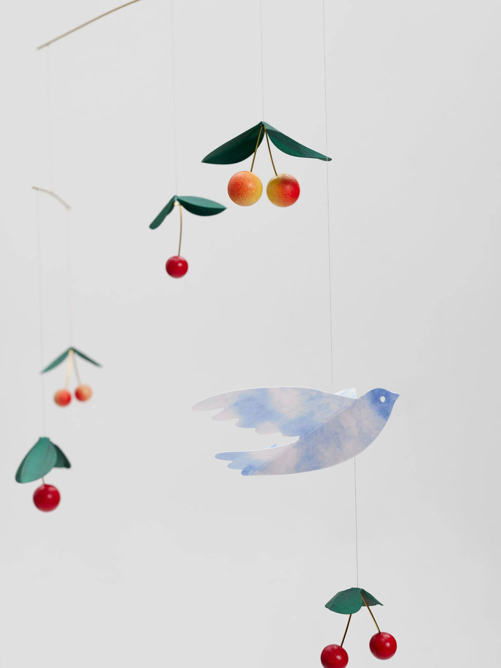 Colourful cherry and bird mobile hanging against a white background