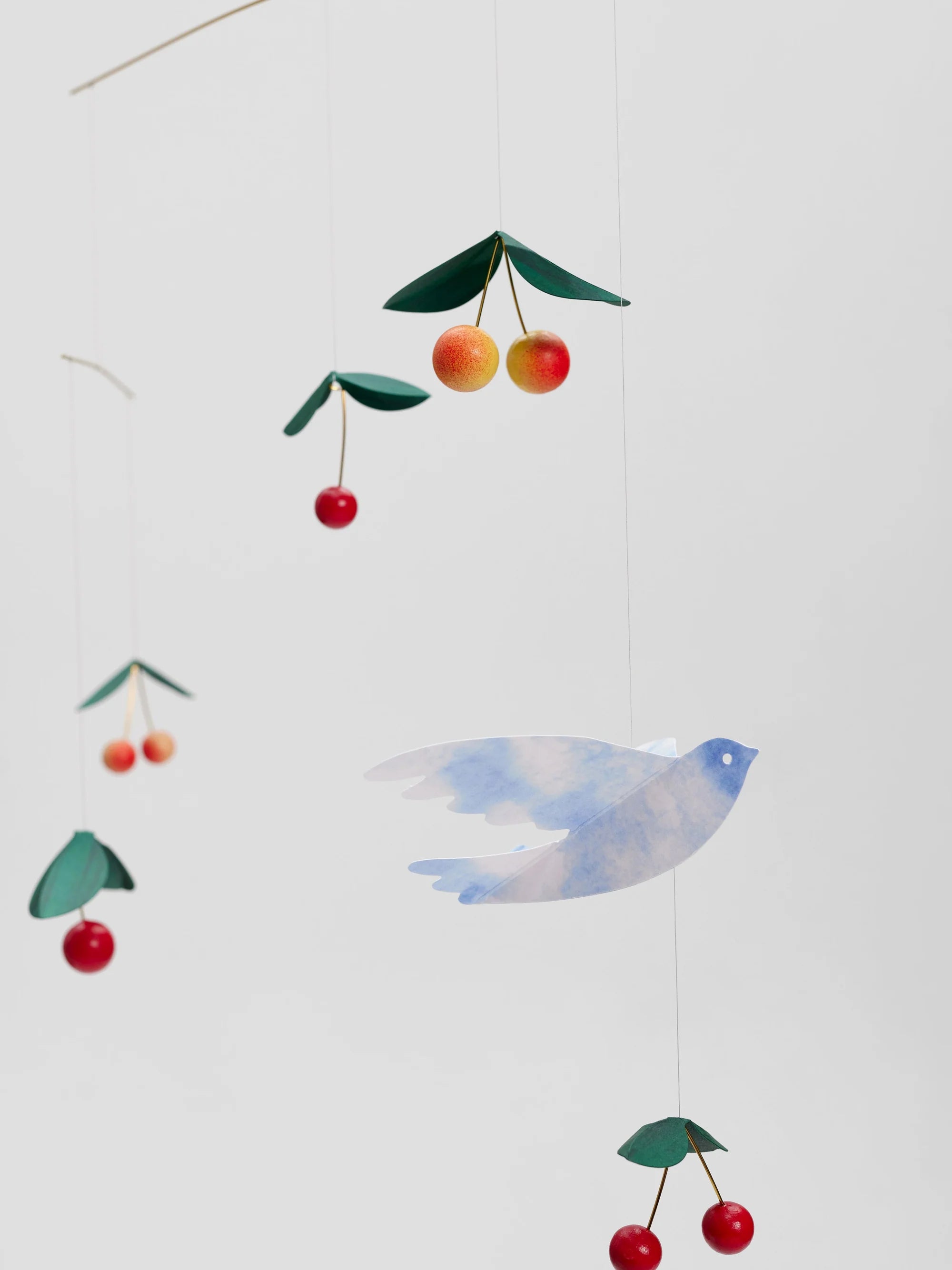Colourful cherry and bird mobile hanging against a white background