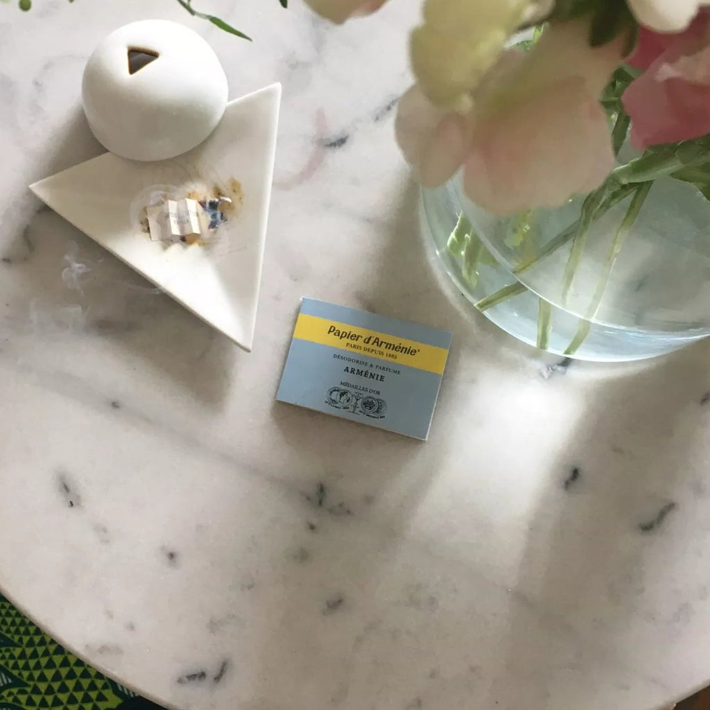 Marble table with decorative items including a vase with flowers, small bowl, and box on a patterned surface. papier d'armenie paper incense