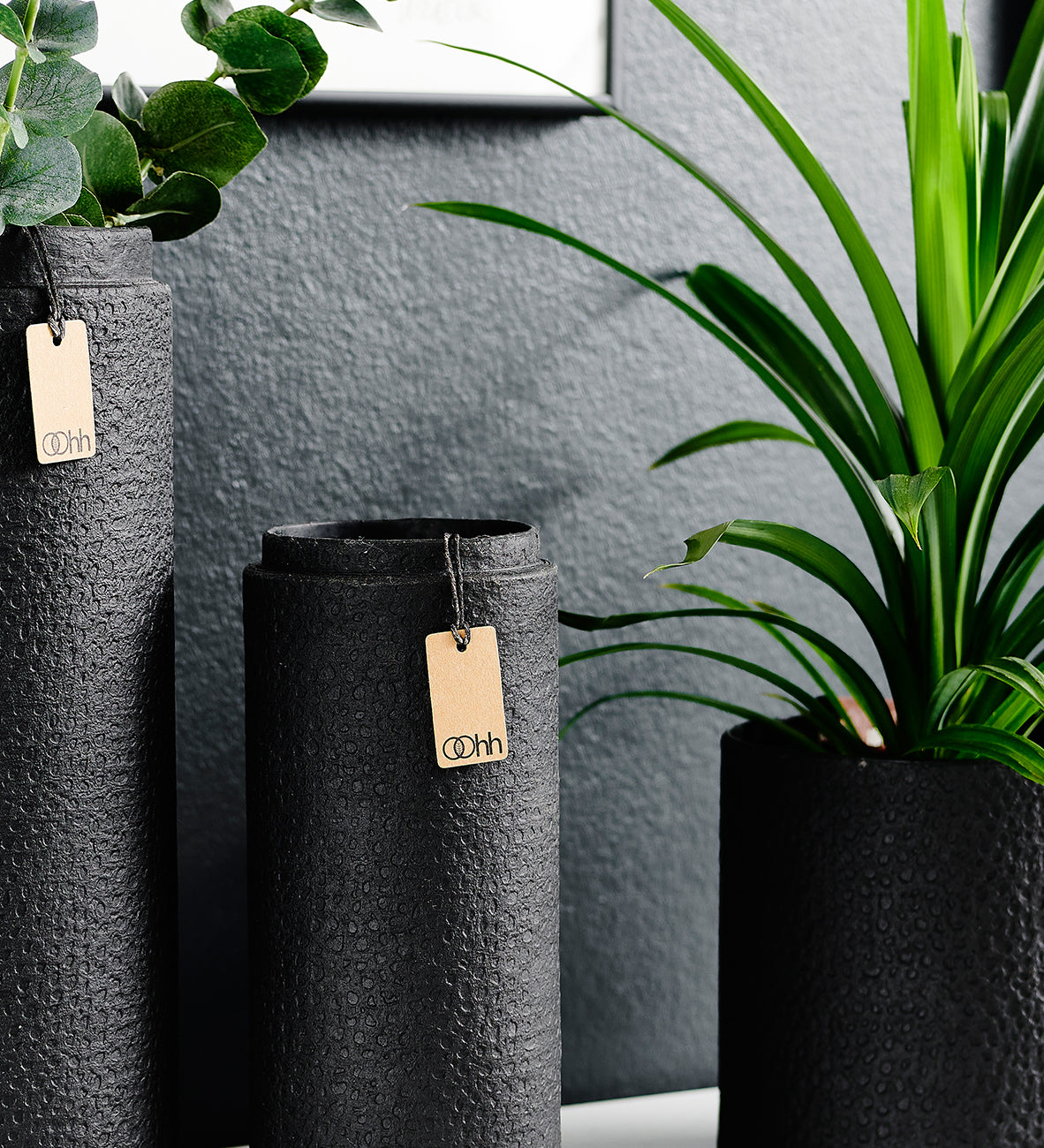 Black textured vases with tags on a gray wall