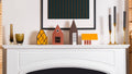Decorative mantel with small Nordic houses, candles, and a framed picture on a white fireplace.