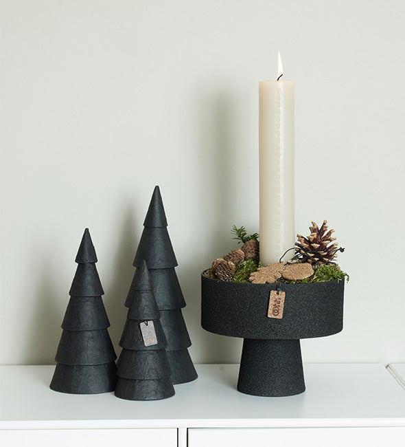Decorative black pedestal bowl with a white candle on a white surface.