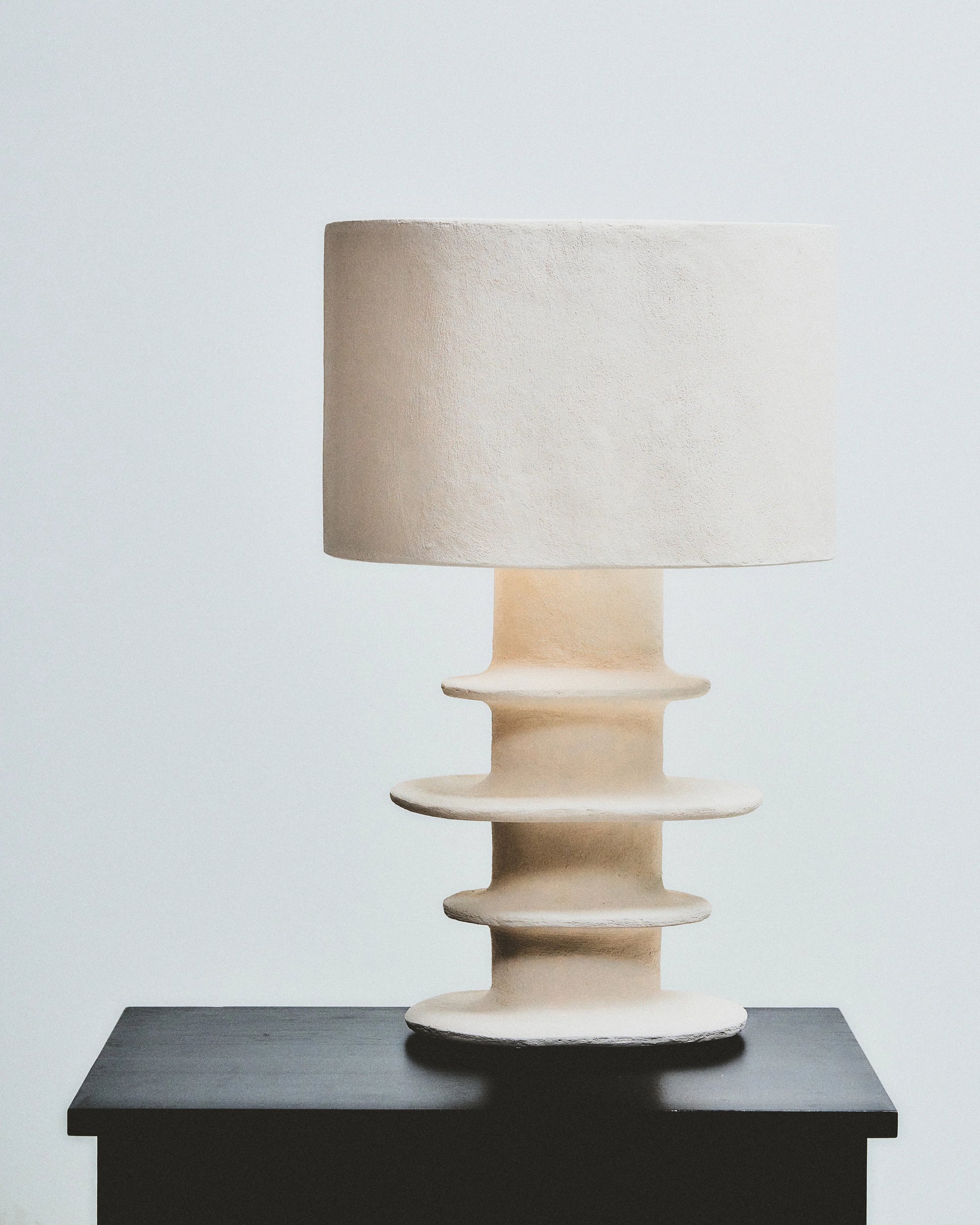 Organic geometrical white paper mache table lamp on a black surface, showcasing innovative design and soft illumination.