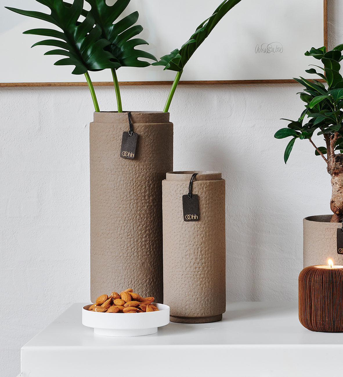 Textured vases with plants and a bowl of nuts on a white surface.