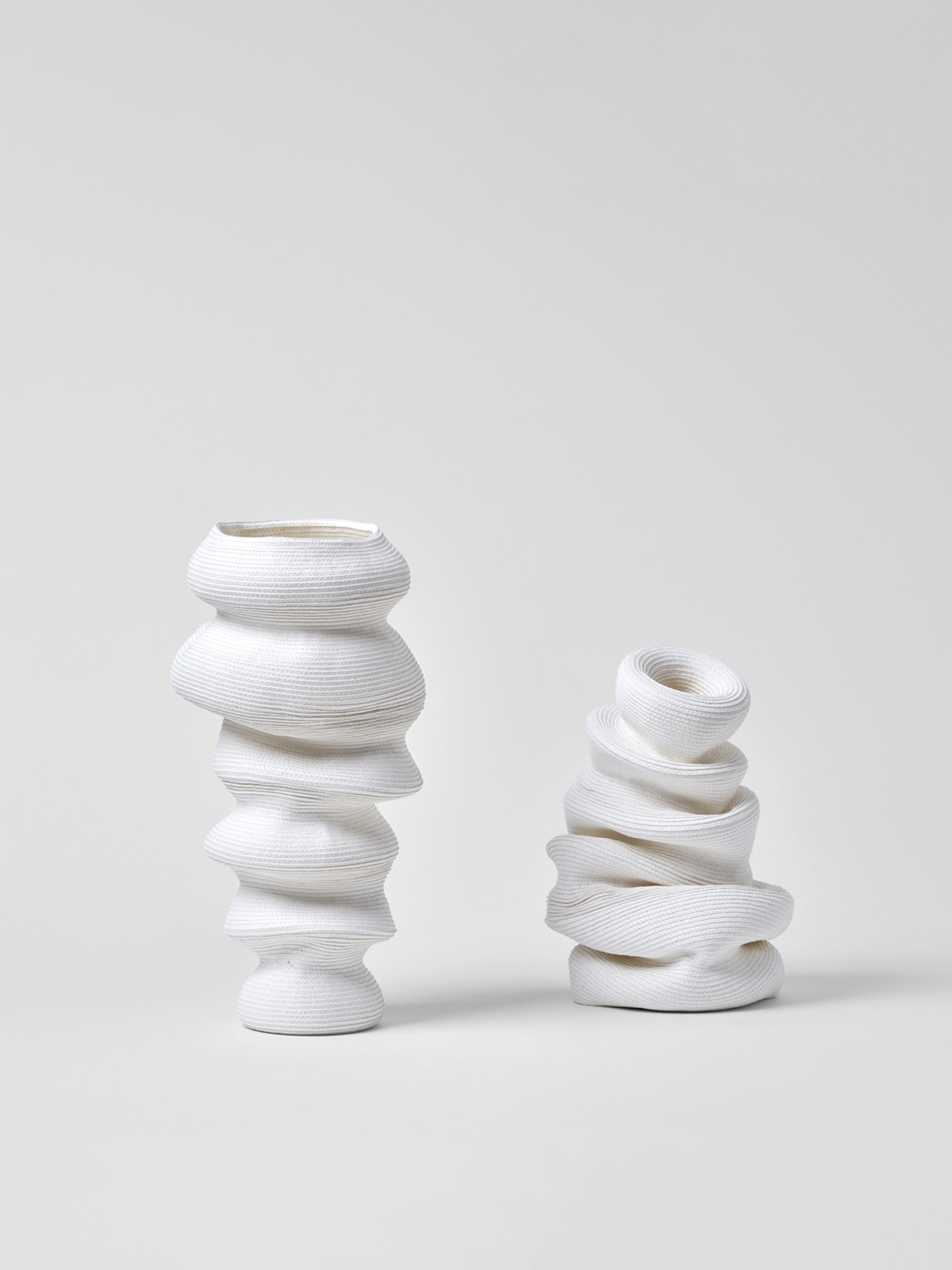 Two white paper vases with twisted design on a light gray background