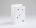 Greeting card with miniature figures of people on skis and snowboards against a white background