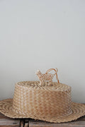 Woven hat with a small decorative cat figure on a plain background