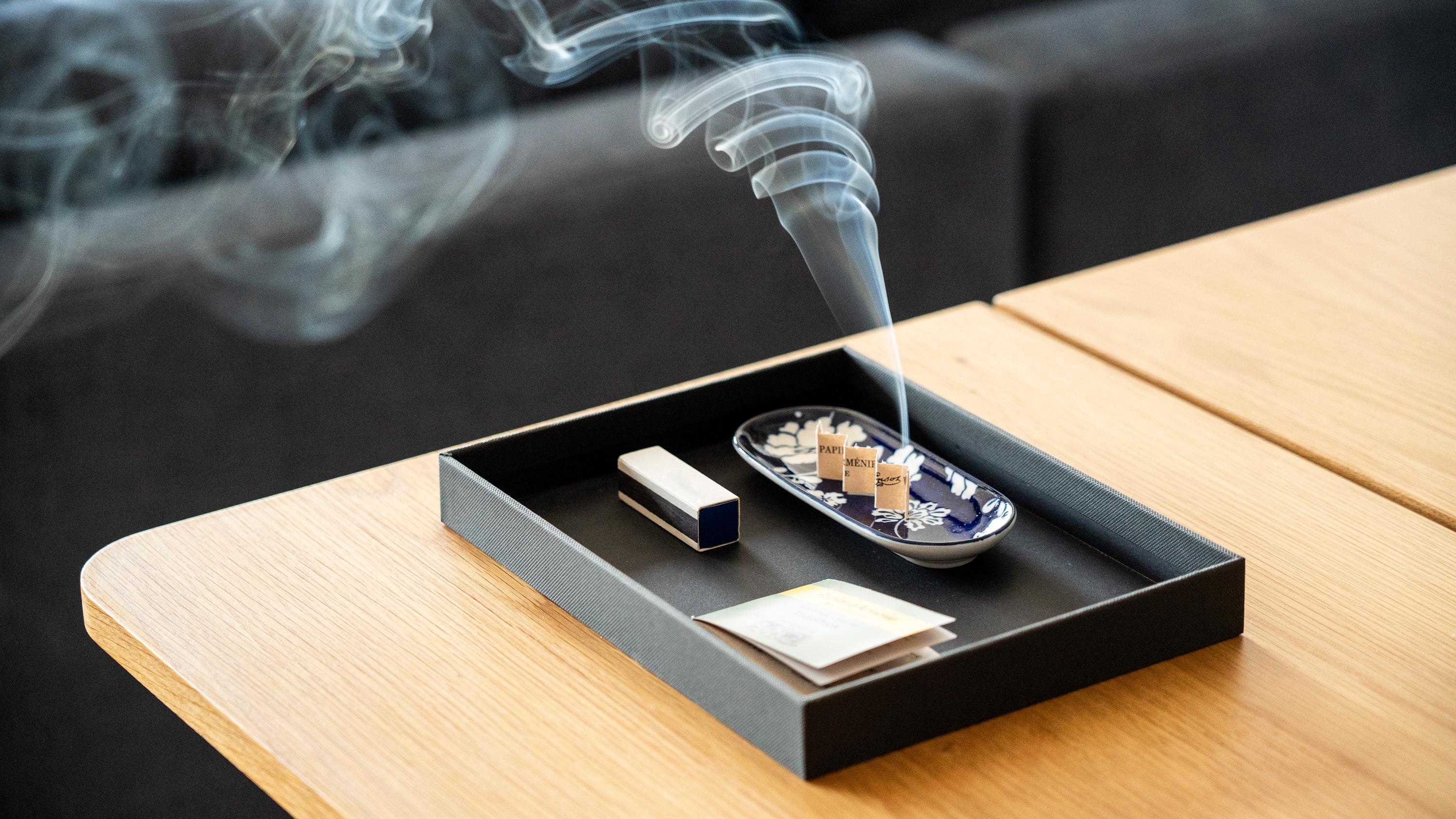 Smoking paper incense on a tray with smoke rising, placed on a wooden surface.
