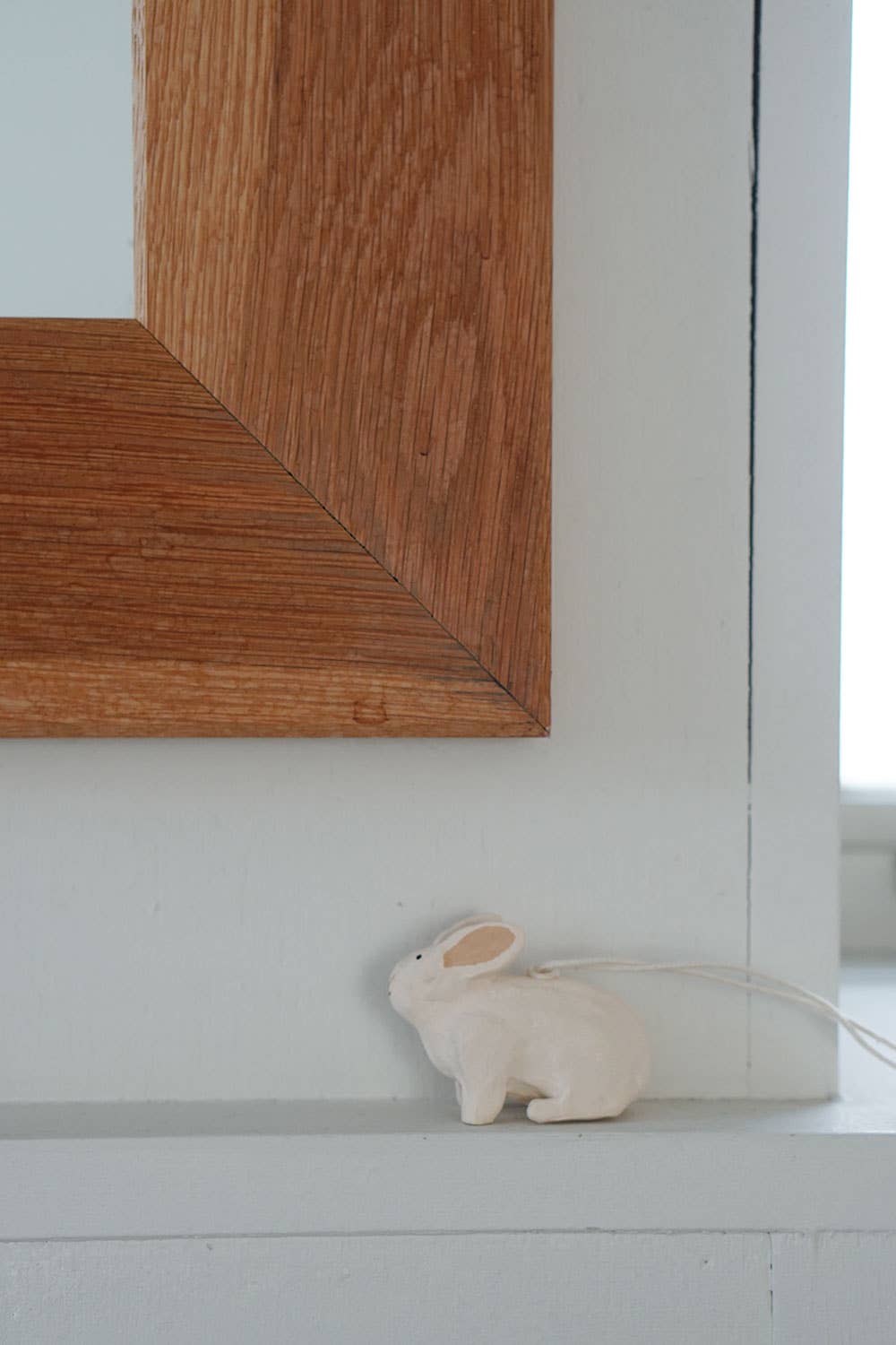 Small white rabbit figurine on a white surface next to a wooden frame.