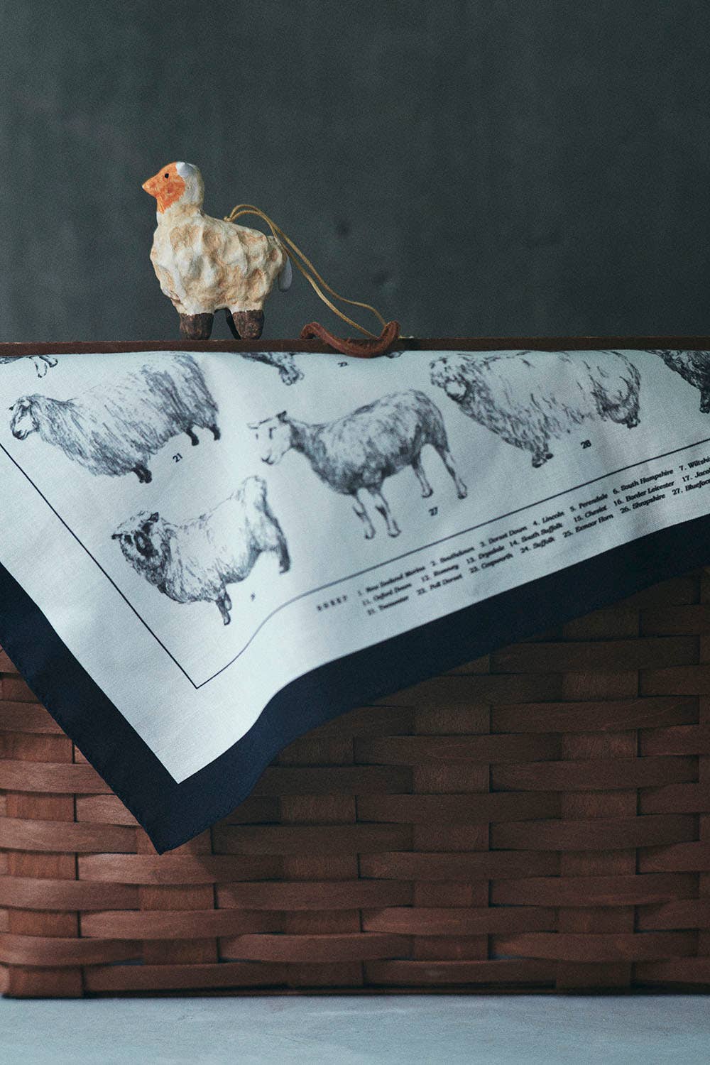 Decorative towel with sheep pattern draped over a wooden basket against a dark background