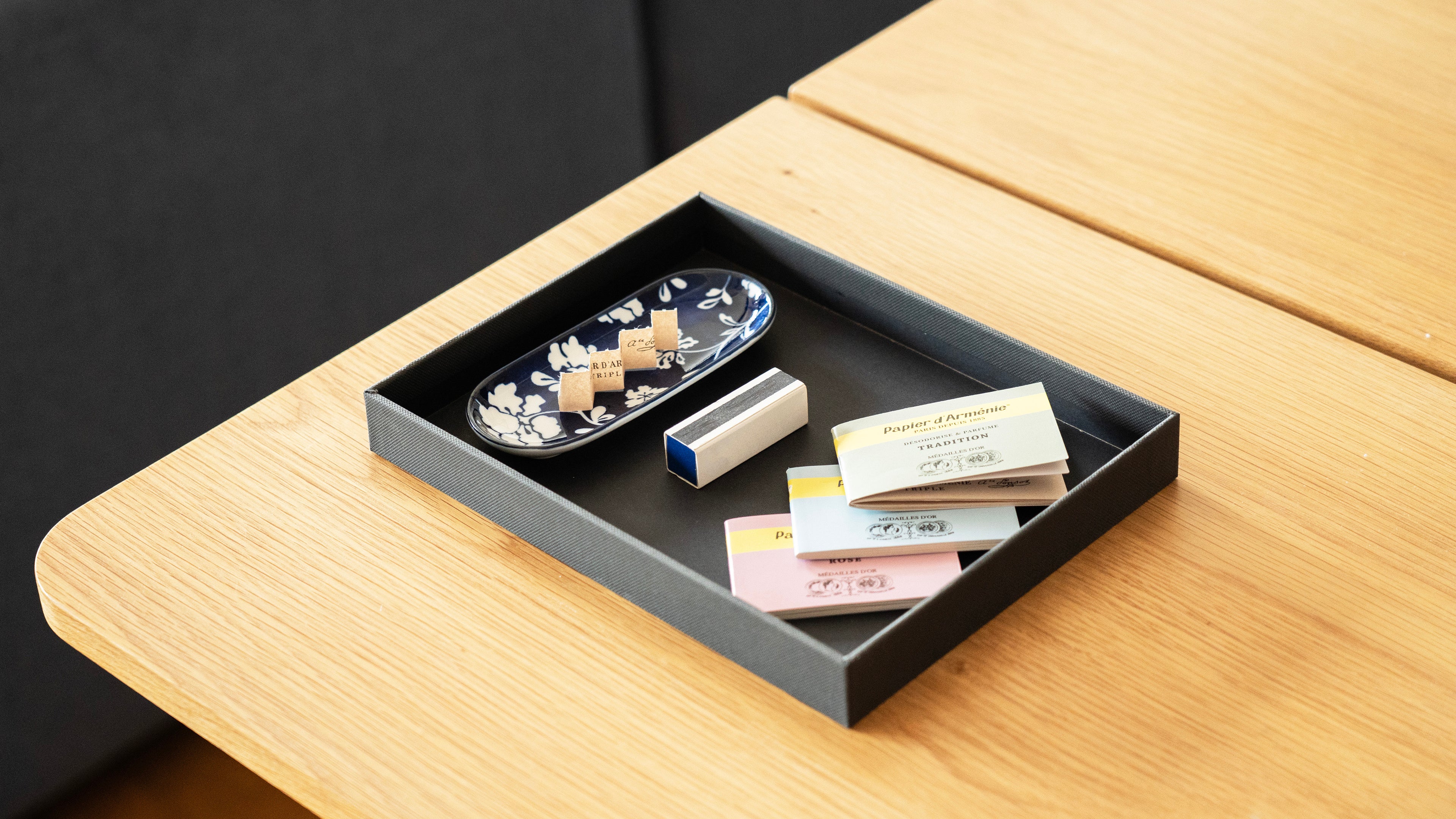 Small black tray with papier d'armenie fragrance booklets on a wooden surface