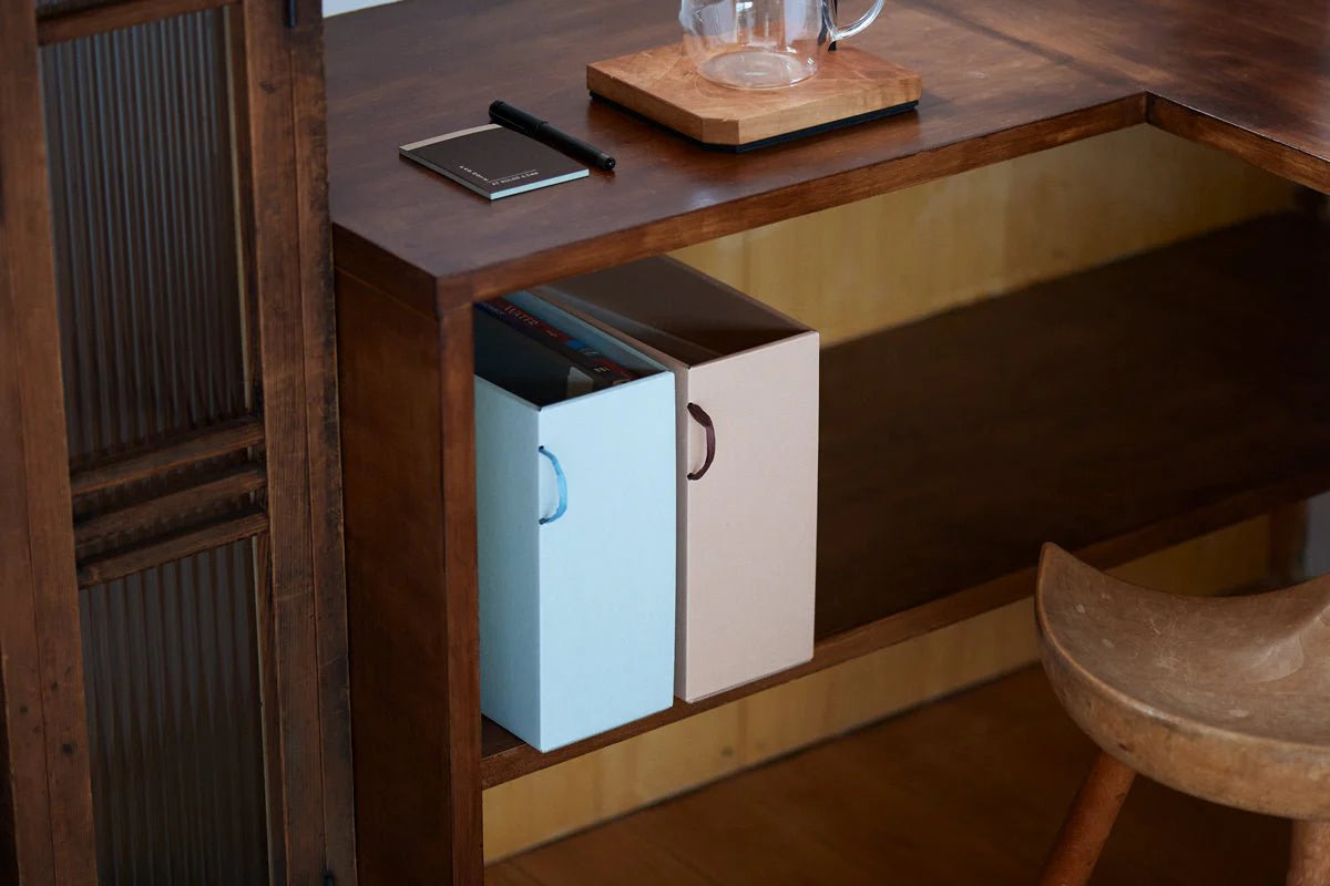 Two small storage boxes in a wooden shelf with a glass on a coaster.